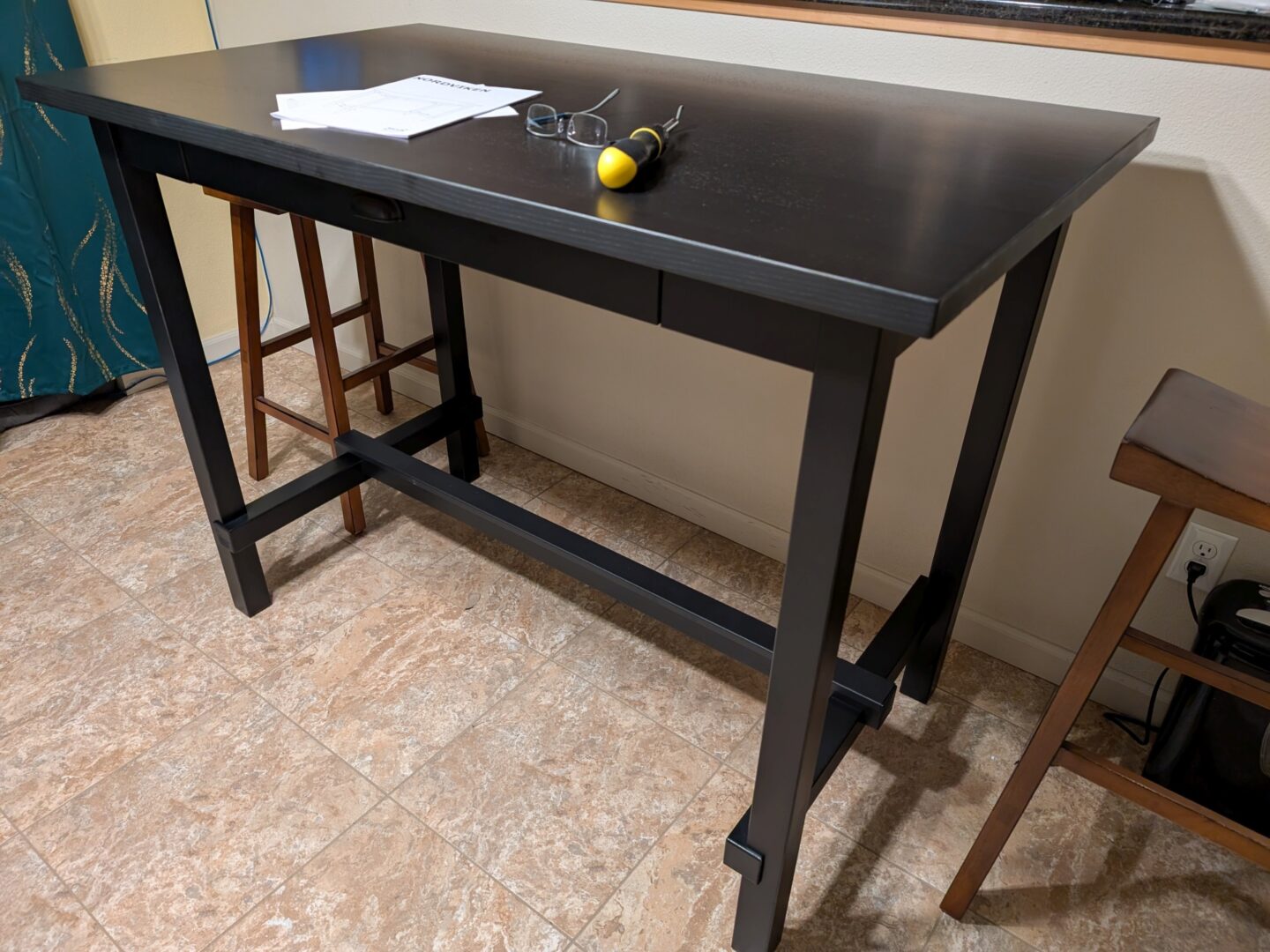 A bar-style dining table flanked by barstools. On its surface are the assembly instructions, a pair of reading glasses, and a screwdriver.