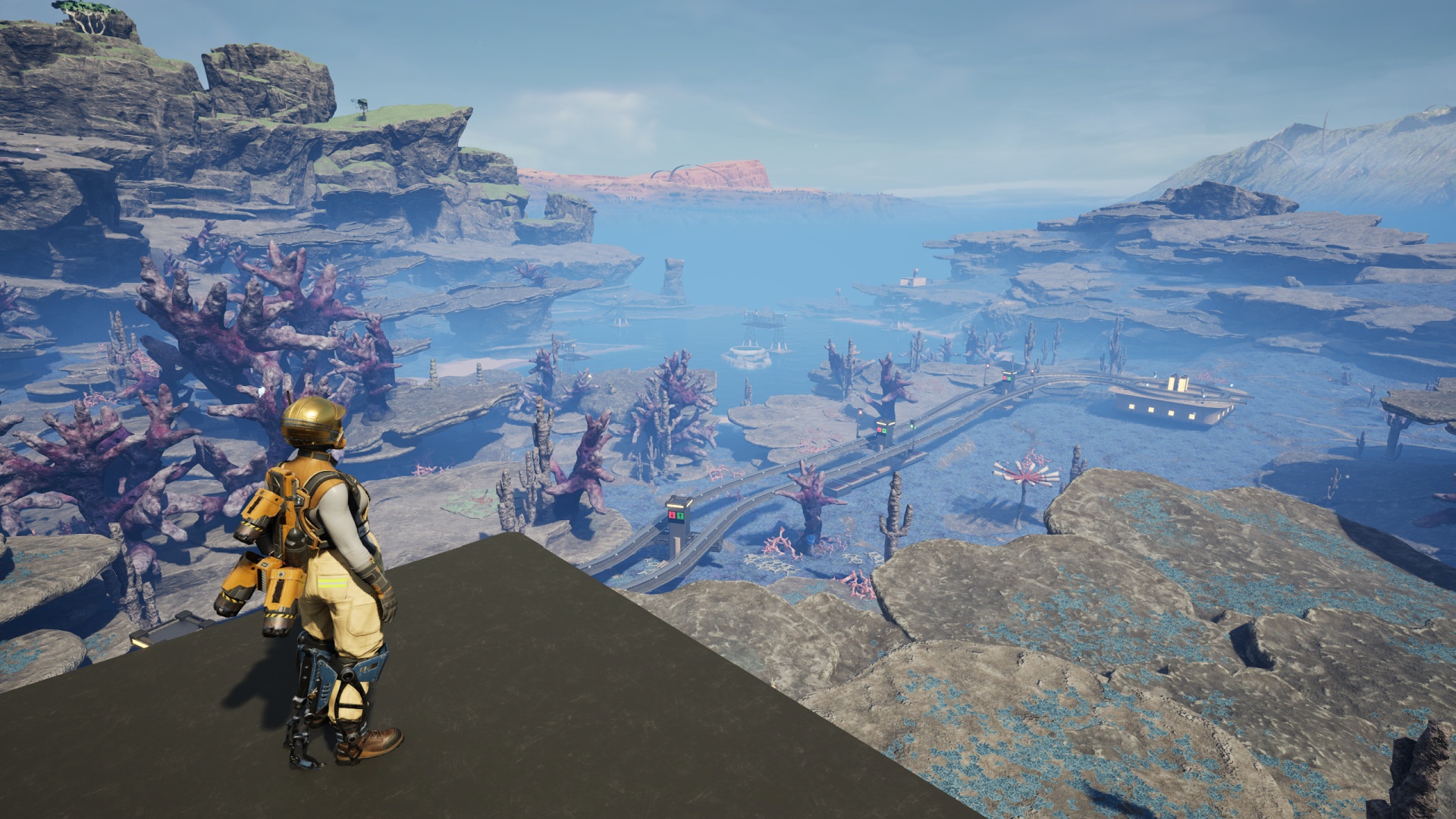 Satisfactory video game screenshot: The Pioneer looks down upon the Blue Crater area, which now features a railway roundabout along with the previously-placed Power Tower network.