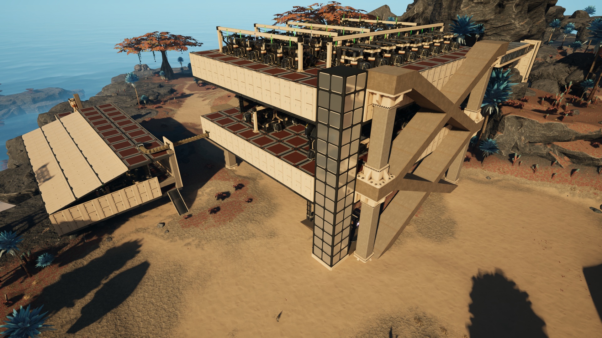 Satisfactory video game screenshot: An aerial view of a large, bulky factory structure consisting of two factory machine floors each with a logistics floor beneath. At the nearest corner is a personnel elevator for ease of access to the various workspaces. Some design elements are in place but the building remains visually unfinished for the time being (awaiting later design pieces).