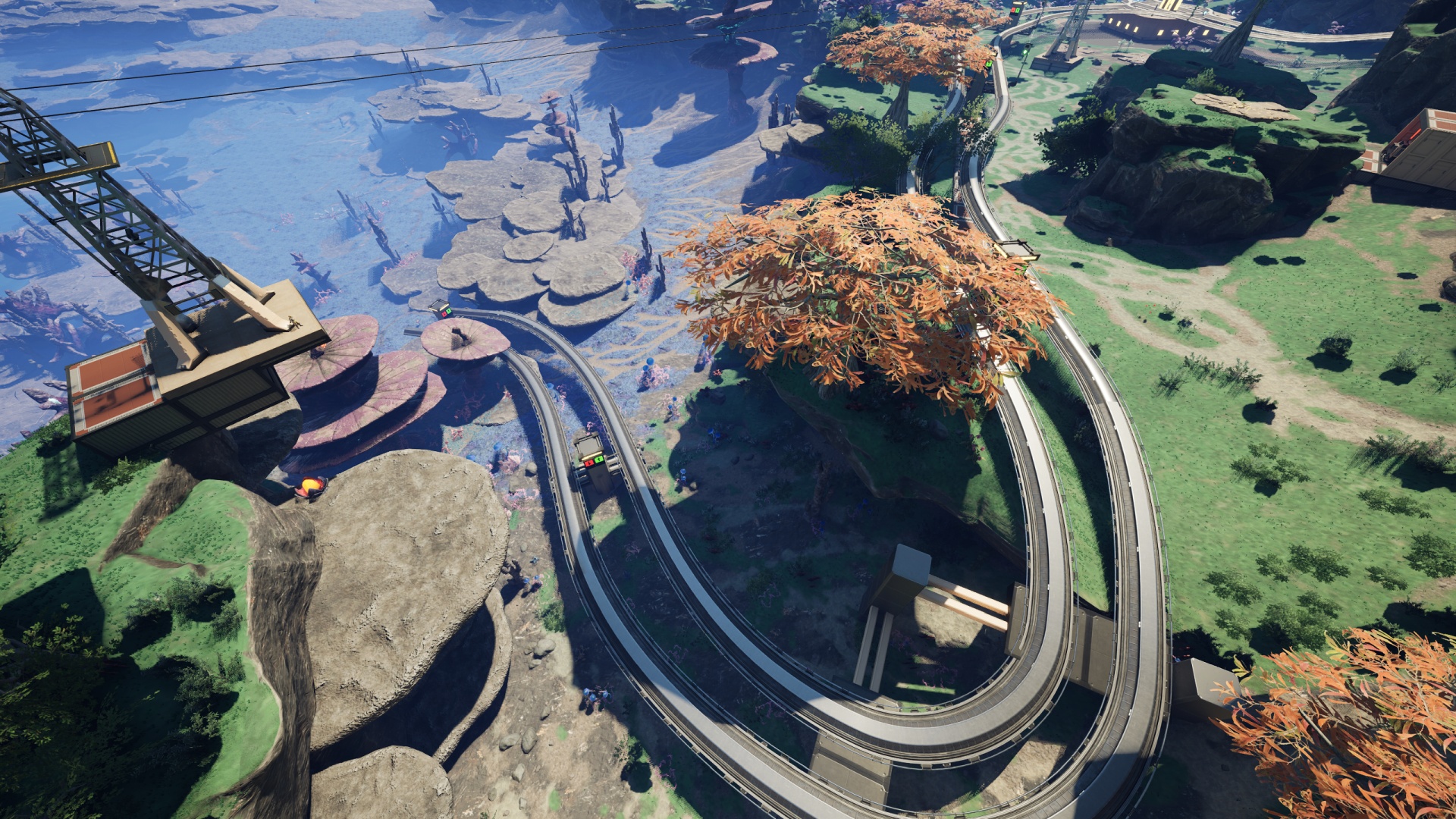 Satisfactory video game screenshot: Paired rail lines route from a roundabout at a small grassy plateau around and down into a blue and gray crater area, the main visual feature of which is the proliferation of fungal-like rock structures.